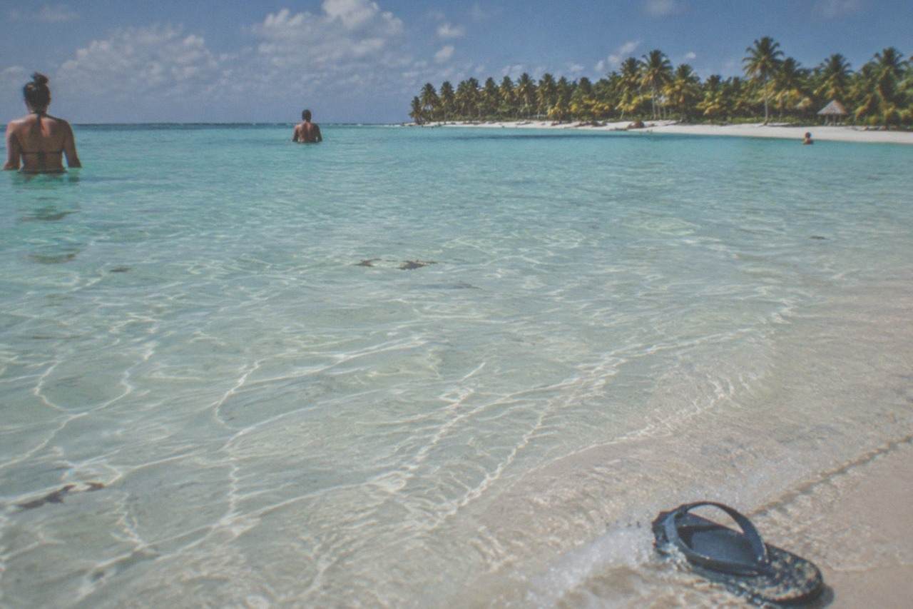 Turquoise shallow water at a tropical sandbar with palm-fringed island shoreline in the distance