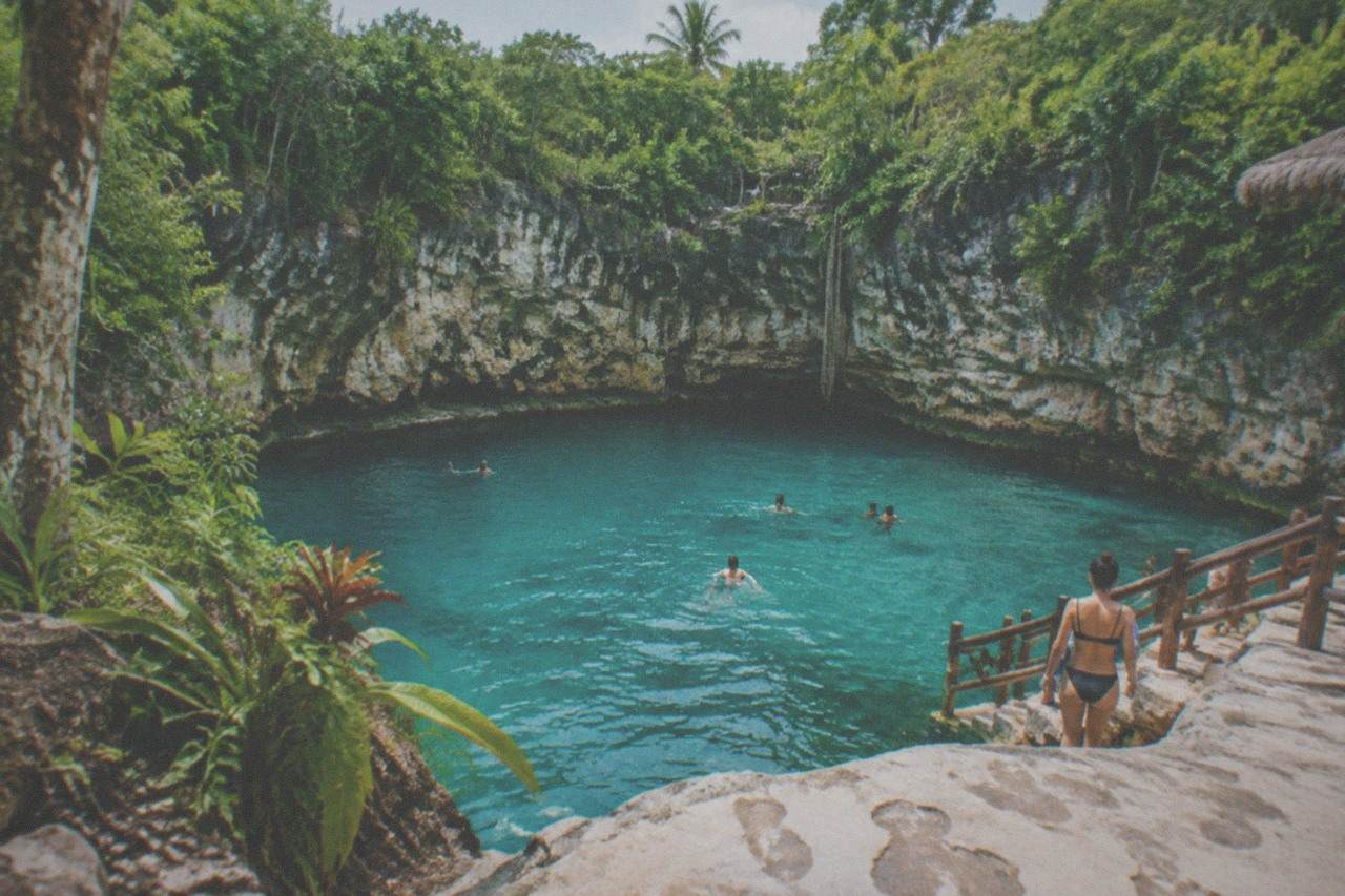 A turquoise freshwater cenote ringed by cliff walls and tropical forest at Scape Park
