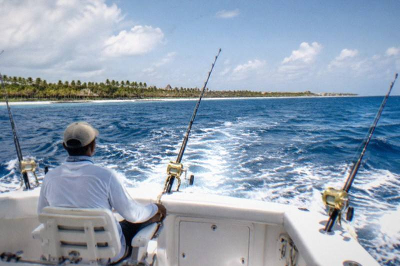 A sport-fishing boat carves through open blue water, trolling lines angled from the outriggers as spray clears the bow.