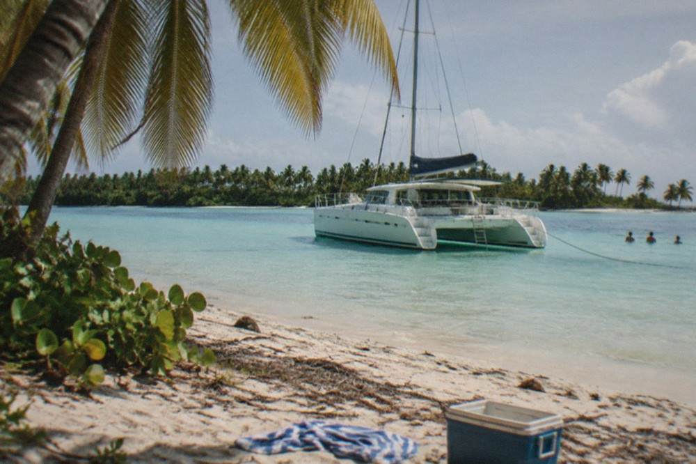 Catamaran moored in shallow turquoise water near a palm-lined beach