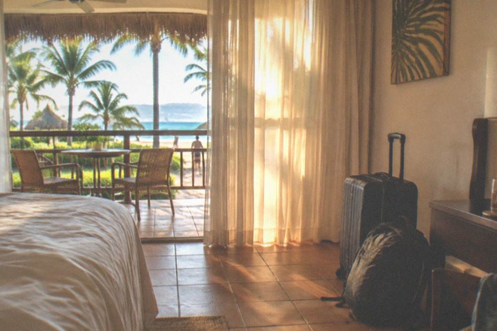 Suitcase and backpack stacked in an open resort room with sunlight through curtains