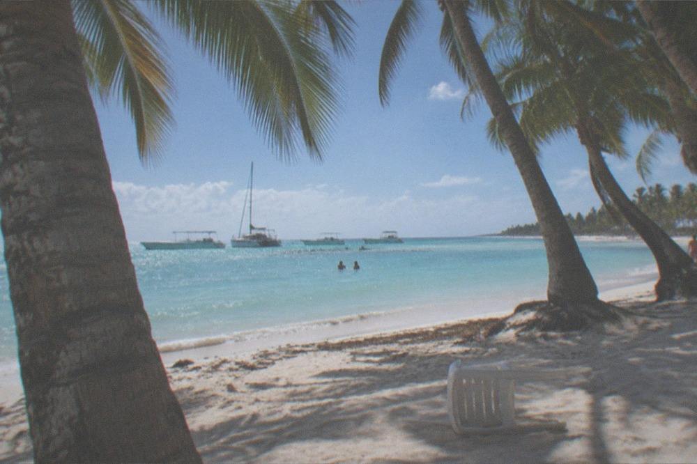 Palm-fringed beach with calm turquoise water and moored excursion boats in the distance