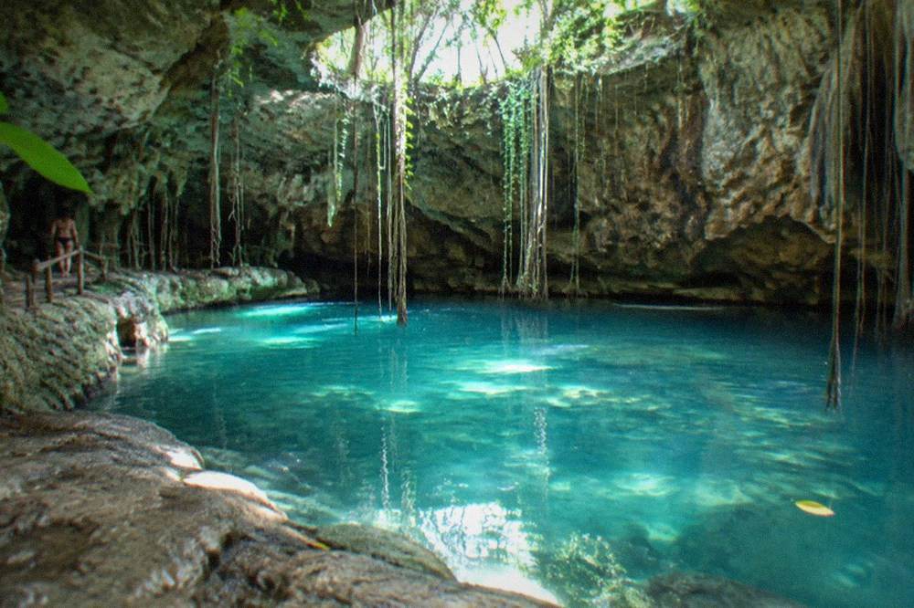 Turquoise freshwater cave pool surrounded by rock walls and hanging vines