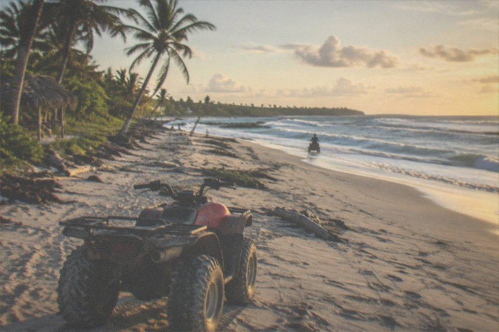 Four-wheeler ATV parked on firm sand at a wide open beach with rolling surf