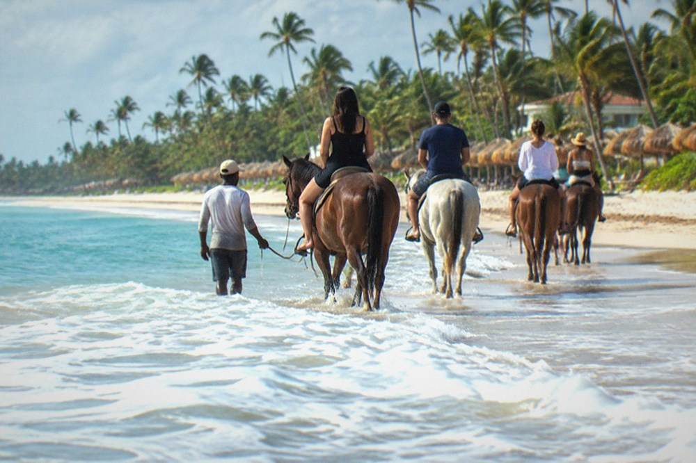 A guide leading a line of horses and riders along the edge of the surf