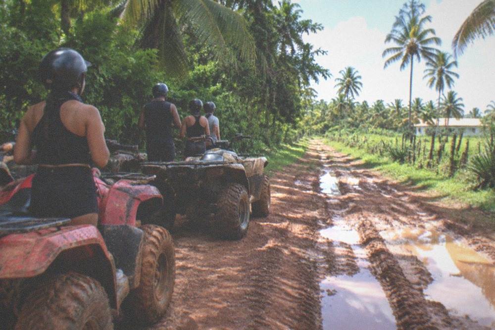 ATV vehicles parked on a dirt track beside tropical vegetation with riders nearby