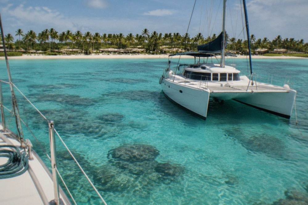 A catamaran moored over pale turquoise shallows with visible coral patches below the surface