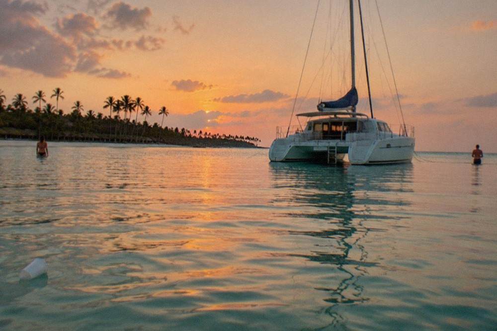 Catamaran anchored at a shallow sandbar as the sky turns orange