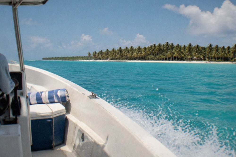 A speedboat cruising across open turquoise water toward a palm-lined island