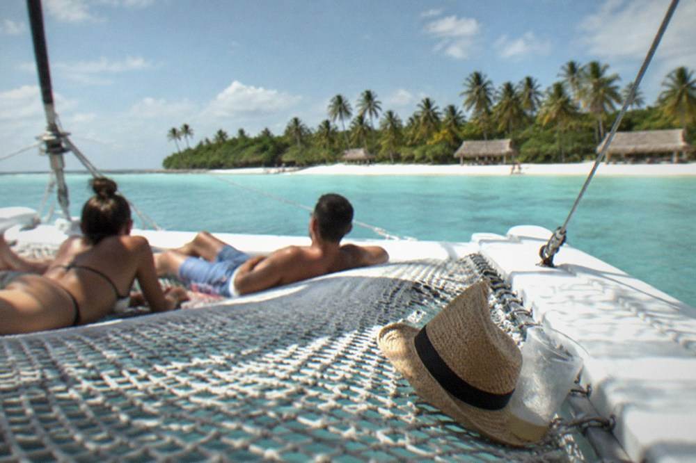 Passengers relaxing on the bow netting of a catamaran in calm blue water