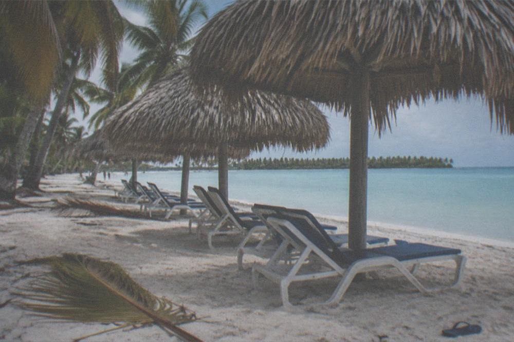 Shaded beach chairs and thatched umbrellas on white sand under palm trees