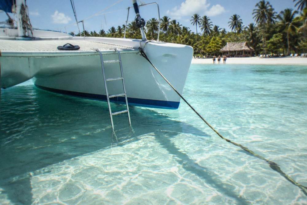 A catamaran moored beside a shallow turquoise sandbar with clear water