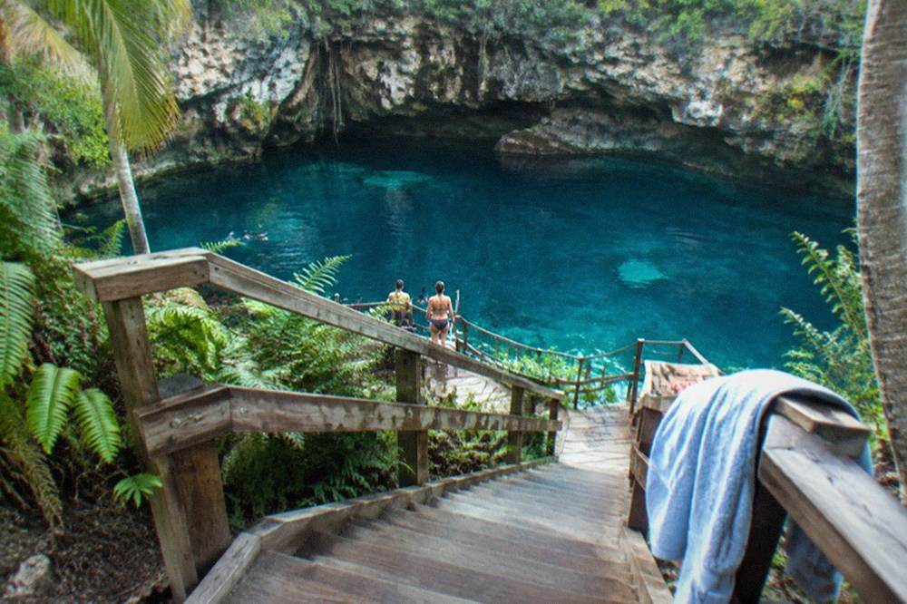 Wooden staircase and walkway descending along a cliff face toward a blue freshwater pool