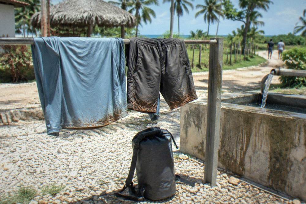 Quick-dry shirt and shorts drying on a railing with a dry bag packed beside them
