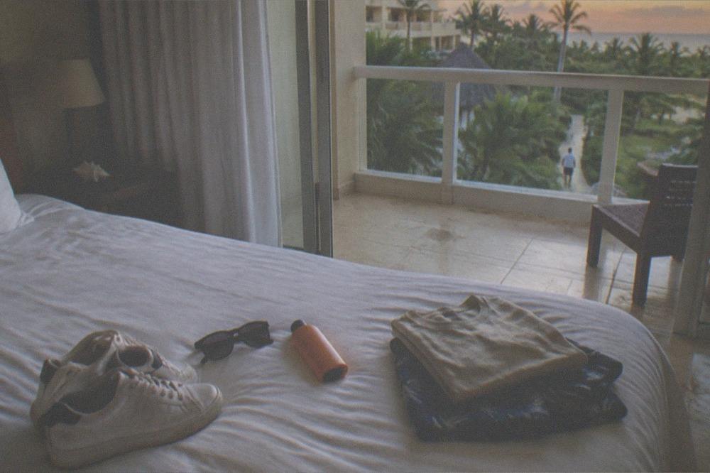 Checklist items laid out on a bed including sneakers, sunglasses, sunscreen and a folded change of clothes